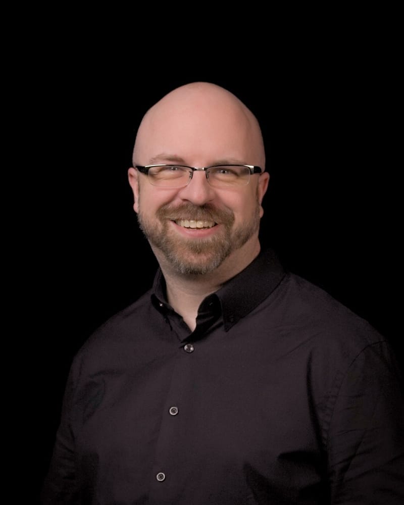 Jeff Neet, smiling, in a dark shirt against a black background